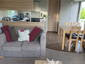 Ein stilvoller Wohnraum mit grauem Sofa, Esstisch aus Holz und Küchenzeile.