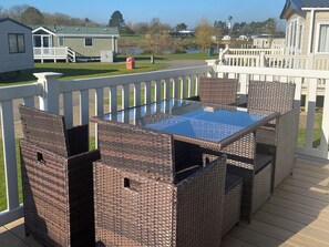 Eine Terrasse mit Korbmöbeln und einem Tisch mit Glasplatte, mit Blick auf eine Wohngegend.