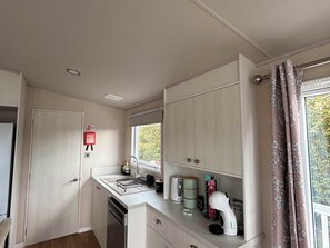 A compact kitchen with a dishwasher, a sink, and a window with curtains. - Primrose Valley Park - Pebbles Retreat (Filey)
