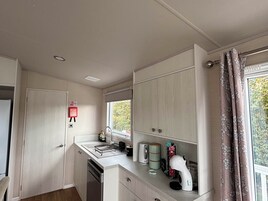 Cocina compacta con lavavajillas, un lavamanos y una ventana con cortinas.
