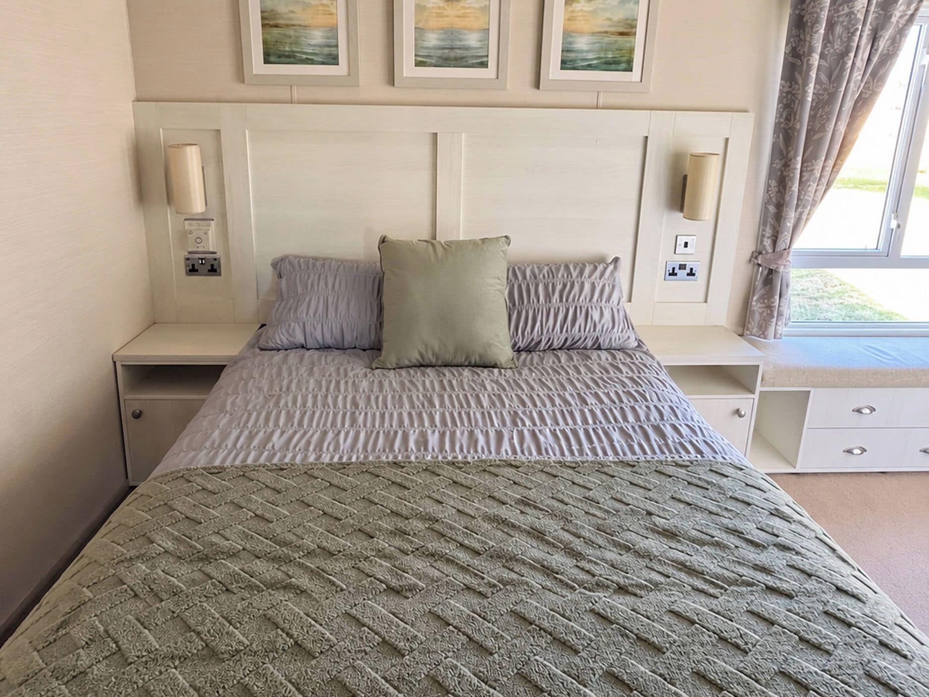 Une chambre d’hôtel comprenant un lit, deux tables de chevet, une commode, une fenêtre avec des rideaux et des lampes fixées au mur.