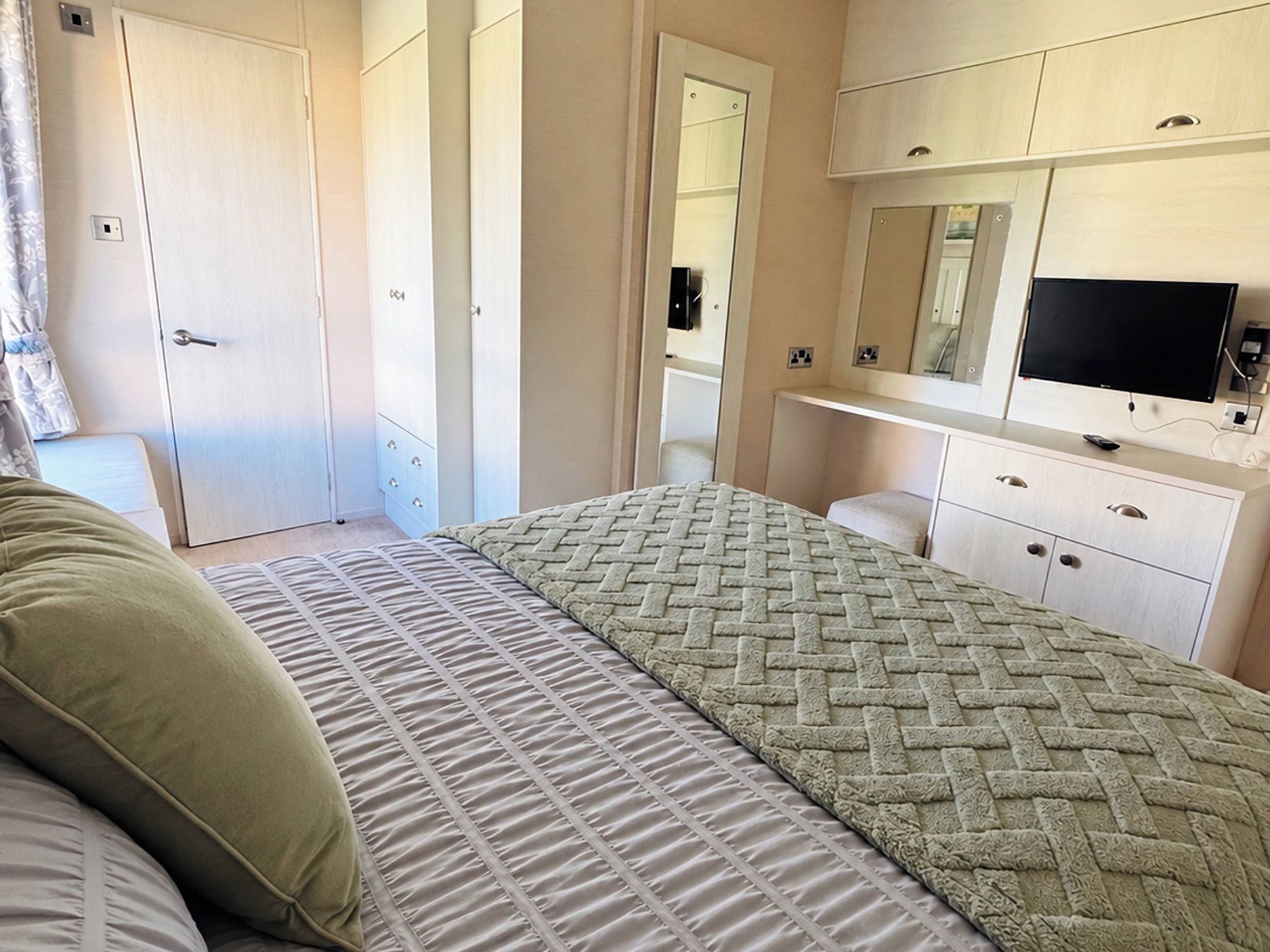 A bedroom with a bed, a dresser, a mirror, and a television.