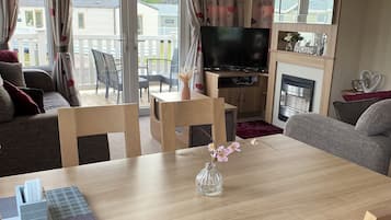 Quarto mobiliado com sofá, mesa de jantar com um vaso, televisão de tela plana e lareira.