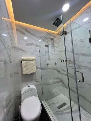 Een moderne badkamer met een douche met glazen wand, een wit toilet en marmeren wanden.