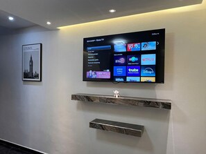 Een wandtelevisie met diverse streamingdiensten, een lijst met een foto van Londen, en twee marmeren planken.