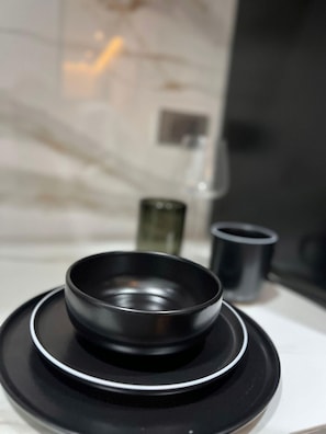 A black bowl on a black plate, with a glass and a black cup in the background.