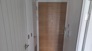 Un couloir avec une porte en bois au fond, des murs blancs et un plancher en bois.