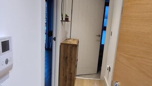 Un couloir étroit au plancher de bois, une porte blanche au fond et un petit meuble en bois.