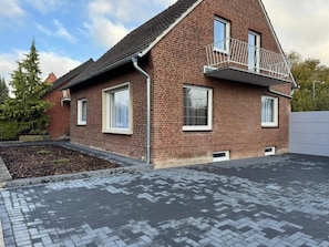 Ein zweistöckiges Backsteinhhaus mit Balkon, großen Fenstern und einer gepflasterten Auffahrt.