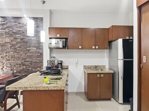 Une cuisine moderne dotée de plans de travail en granit, d’armoires en bois, d’un four à micro-ondes encastré et d’un réfrigérateur en acier inoxydable.