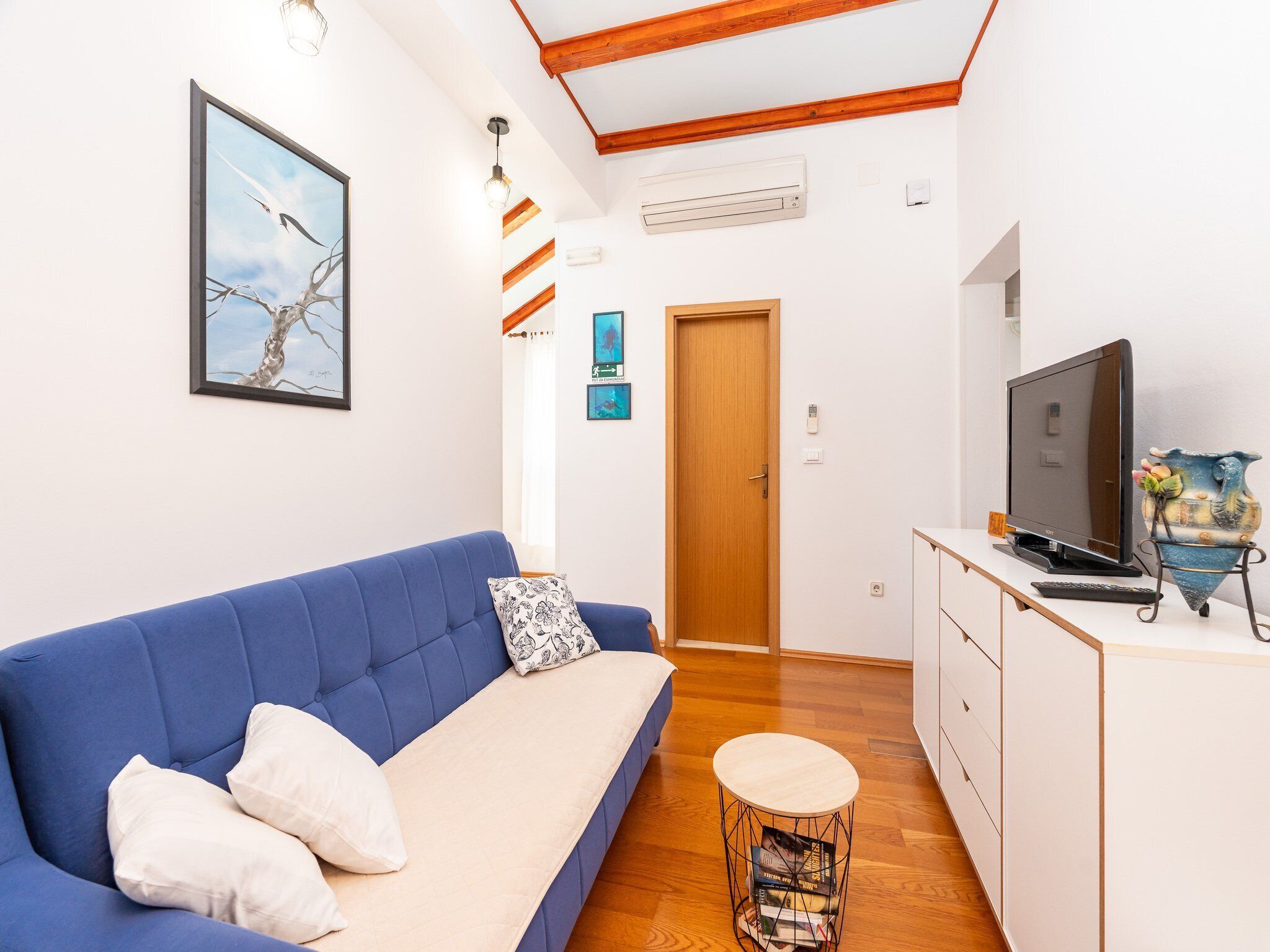 Una sala moderna con un sofá azul, un televisor, una mesita redonda y un aparador de madera.