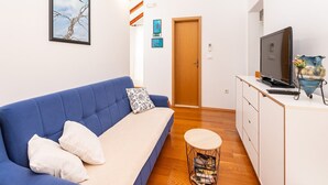 Una sala moderna con un sofá azul, un televisor, una mesita redonda y un aparador de madera.