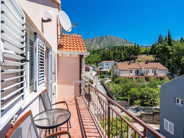 A balcony with a table and chairs, a satellite dish, and a view of a hillside with houses. - Villa Seka Mlini (Zupa dubrovacka)