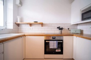 Cozinha com armários brancos, bancada de madeira, forno embutido e micro-ondas acima.