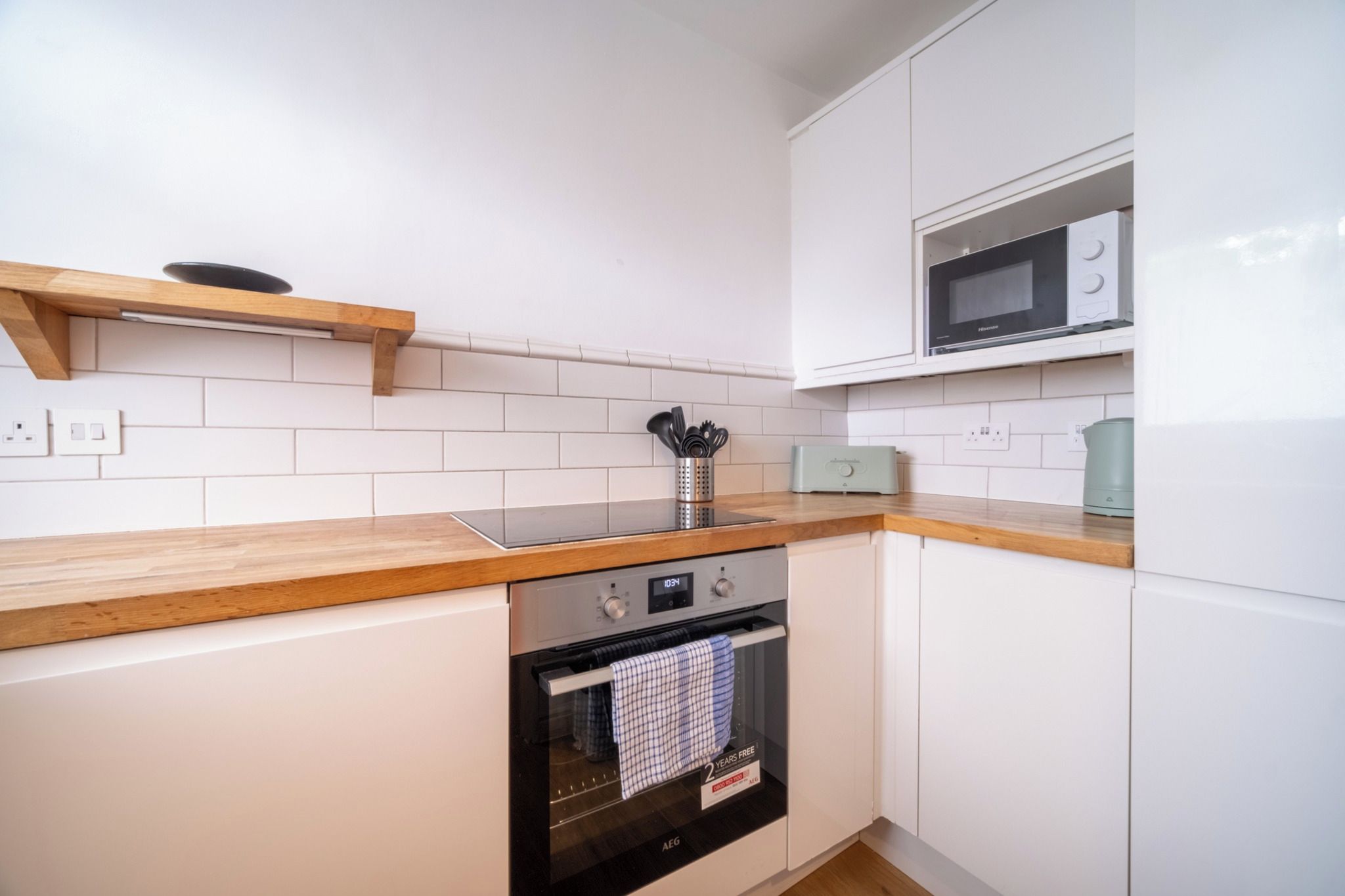 A compact kitchen with white cabinets, a wooden countertop, a built-in oven, and a microwave above it.