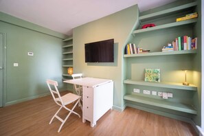 Quarto com escrivaninha, cadeira, estante e televisão na parede.