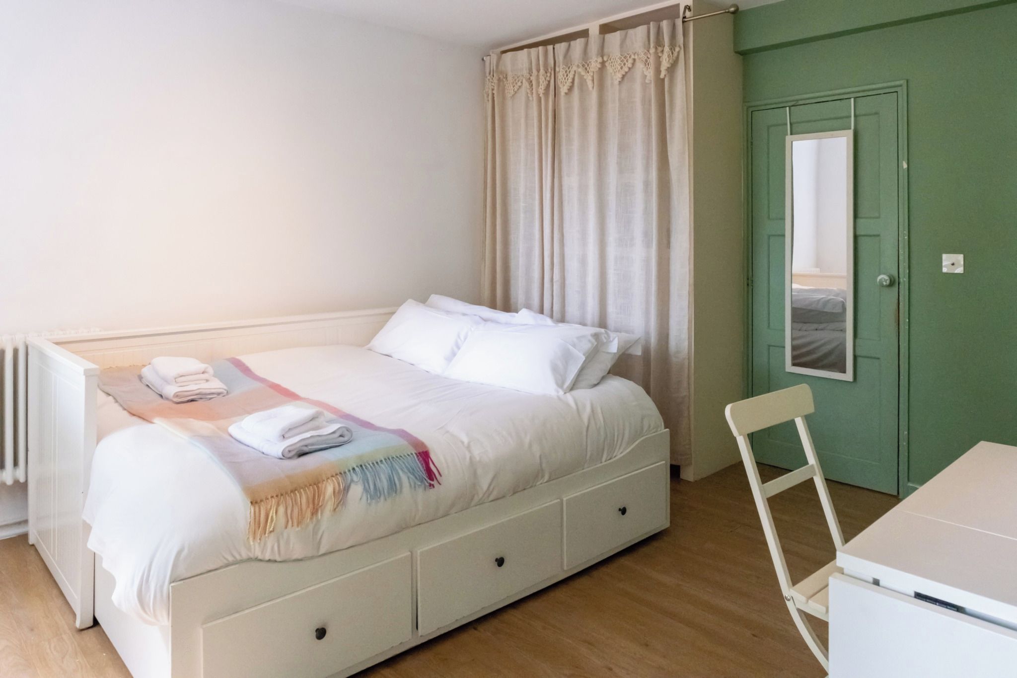 Une chambre avec un lit simple, une table de chevet, une chaise et une porte dotée d’un miroir.