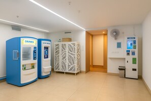 Eine helle, moderne Lobby mit einem blauen Getränkeautomaten, einem weißen Eiswasserausgeben und einem Möbelstück mit Muster sowie einer öffentlichen Toilette.