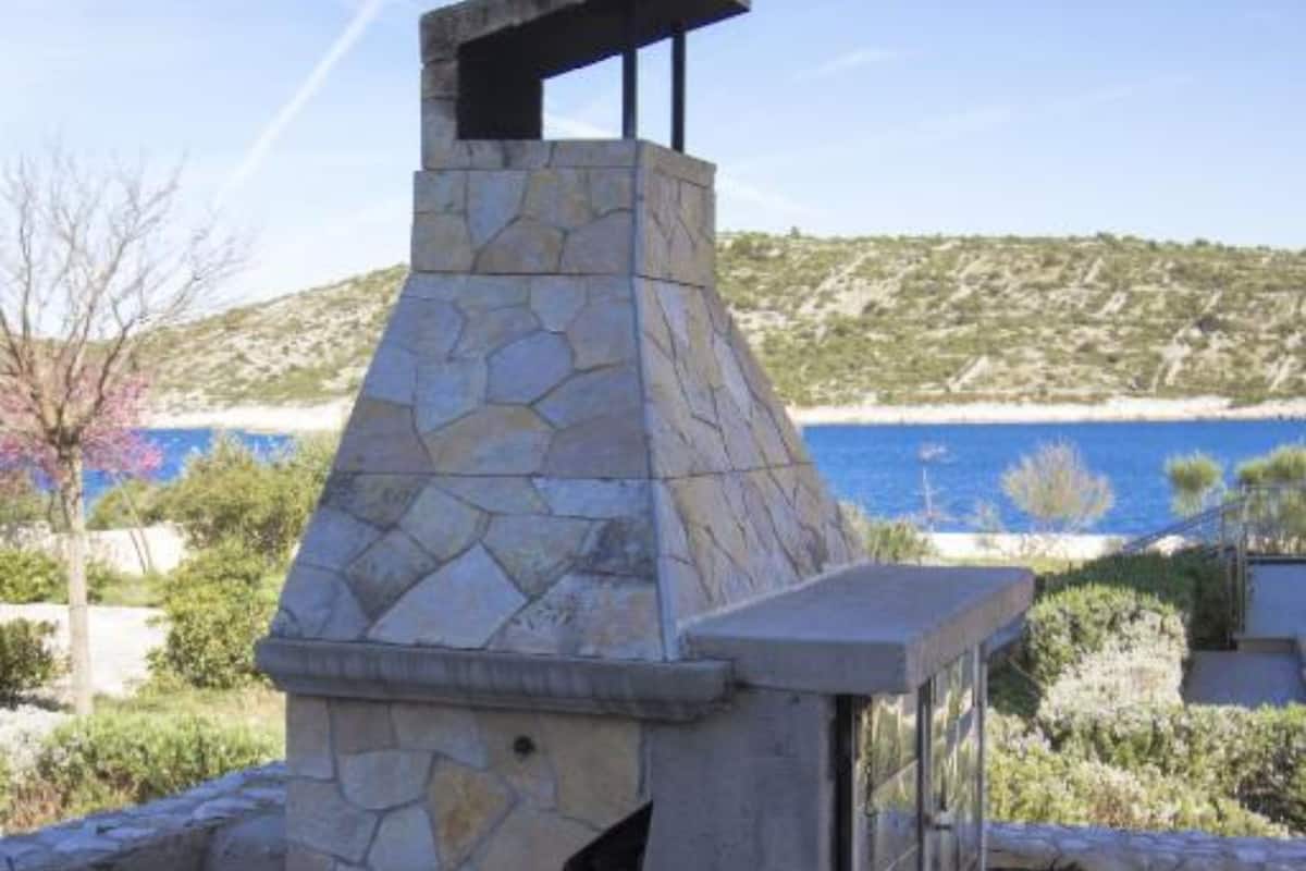 A stone-built outdoor structure with a chimney, overlooking a coastal landscape with a clear view of the sea and hills.