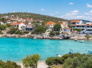 A coastal town with buildings along the shore, clear turquoise water, and boats. - Villa Ivan (Rogoznica)
