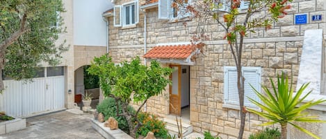 A stone building with a tiled roof, a small garden with flowers and shrubs, and a sign indicating it is an apartment.