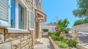A stone building with a stone pathway leading to a wooden door, surrounded by greenery and potted plants. - Secret Garden Apartment Žarka (Postira)