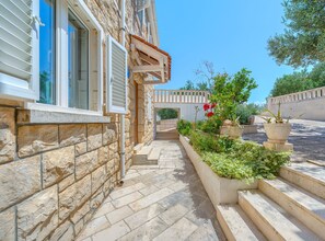 A stone building with a stone pathway leading to a wooden door, surrounded by greenery and potted plants. - Secret Garden Apartment Žarka (Postira)