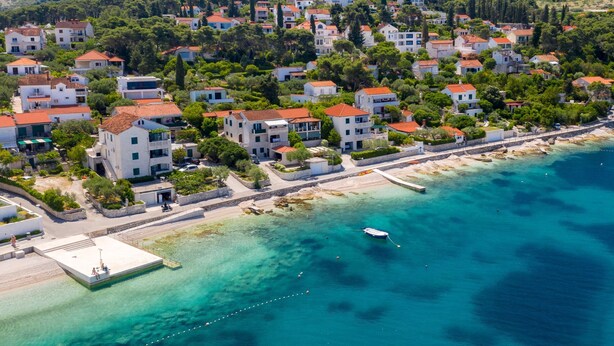 An aerial view of a coastal residential area with houses, a clear blue sea, and a pier. - Secret Garden Apartment Žarka (Postira)