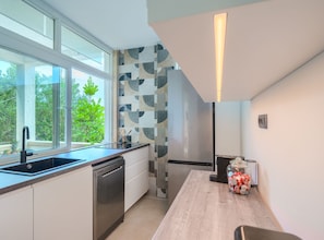 Eine moderne Küche mit Geschirrspüler, Kühlschrank, einem Fenster mit Blick auf Grünflächen und einem Holztisch mit einer Dose Snacks.