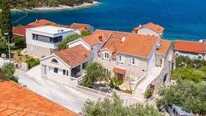 A coastal residential area with houses featuring red-tiled roofs and stone walls, overlooking a clear blue sea. - Secret Garden Apartment Žarka (Postira)