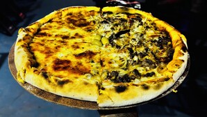 A pizza on a wooden board held by a person with a tattooed arm. - Pousada 100 Passos (Tamandaré)
