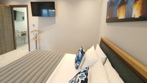 Ein modernes Hotelzimmer mit einem Bett, einem an der Wand montierten Fernseher und einem Gemälde eines Dorfes.