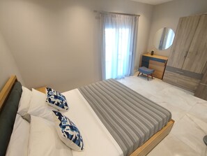 Ein Schlafzimmer mit einem Bett, einem Nachttisch, einem Sessel, einem Kleiderschrank und einem Fenster mit Vorhängen.