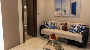 Ein modernes Wohnzimmer mit einem Glastisch, einem beigen Sofa mit gemusterten Kissen und einer Wand mit drei gerahmten Kunstwerken.