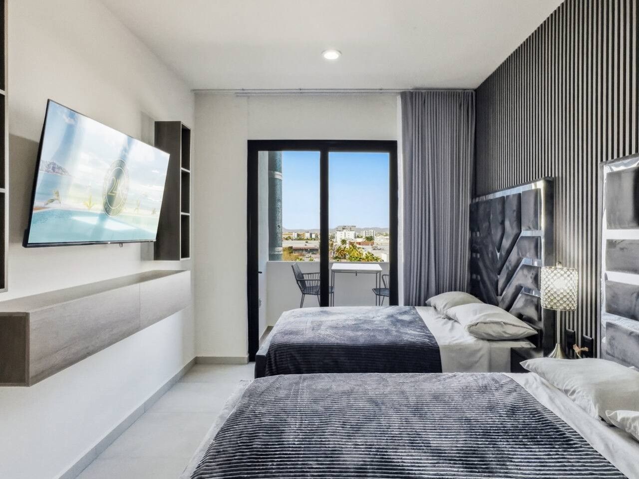 A modern bedroom with a bed, a TV mounted on the wall, and a balcony with a view.