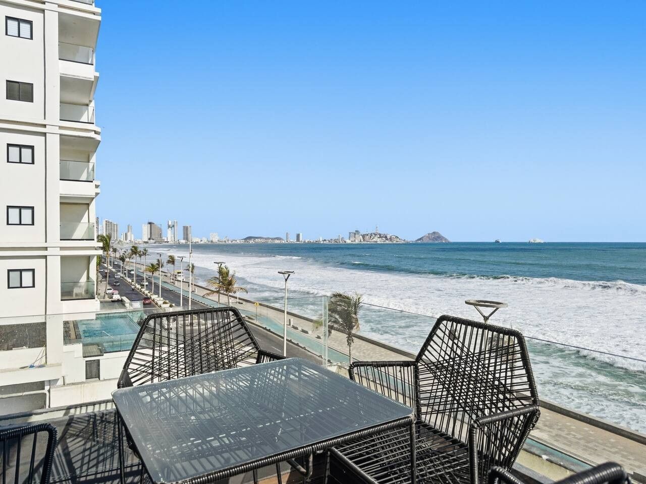 Un balcon avec une table et des chaises donnant sur une plage et l’océan.