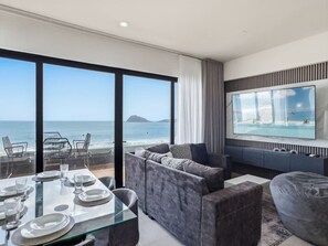 Ein modernes Wohnzimmer mit großem Fernseher, Sitzgelegenheiten und Blick auf den Ozean.