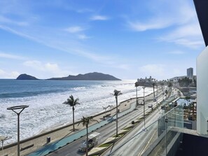 Una carretera costera con piscina, palmeras y vistas al océano y montañas lejanas.