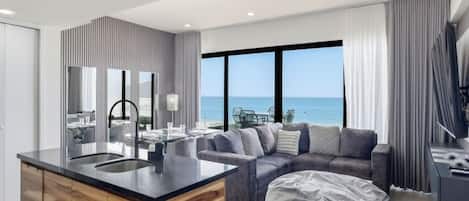 A modern living room with a large window, a sofa, a coffee table, and a kitchen area with a wooden island.