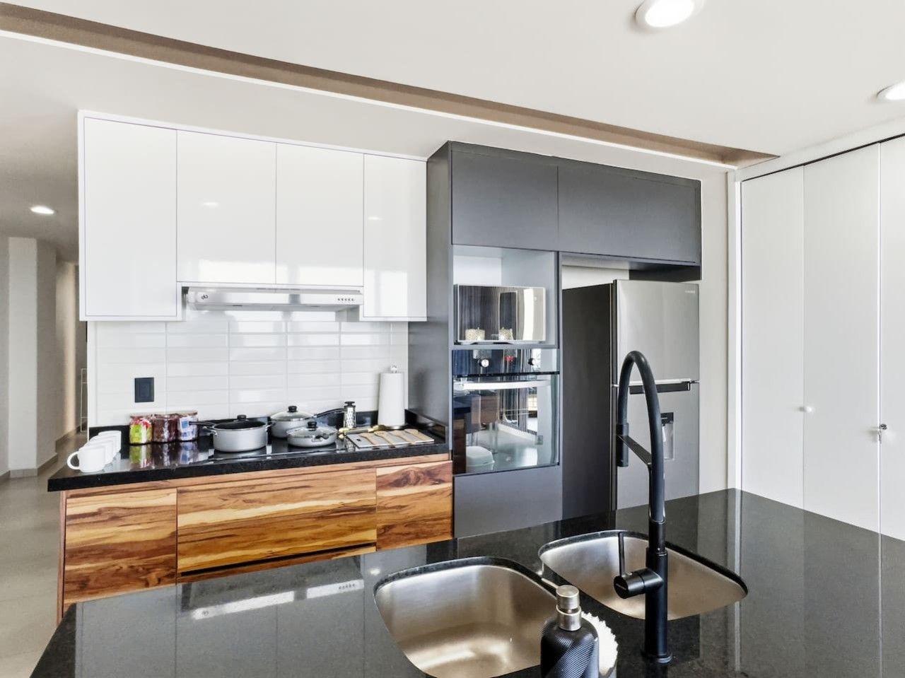 A modern kitchen with white cabinets, a wooden countertop, a black faucet, and a stainless steel sink.