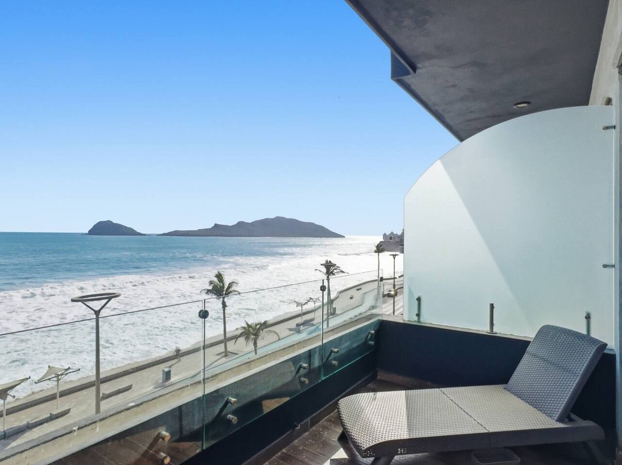 A balcony with a view of the beach and ocean, a seating area with a chair, and a railing.