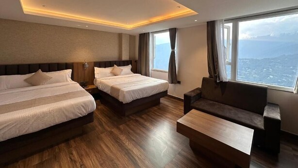 Ein Hotelzimmer mit zwei Betten, einem Sofa, einem Couchtisch und einem großen Fenster mit Blick auf die Stadt.