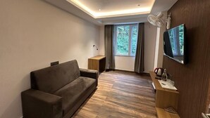 Ein modernes Wohnzimmer mit einer Couch, einem an der Wand montierten Fernseher, Holzboden und einem Fenster mit Vorhängen.
