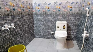 Un bagno con il water, un secchio giallo e una doccia.