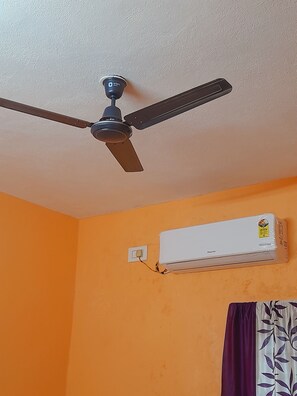 Ein Deckenventilator, eine Klimaanlage und eine Steckdose an einer orangefarbenen Wand.