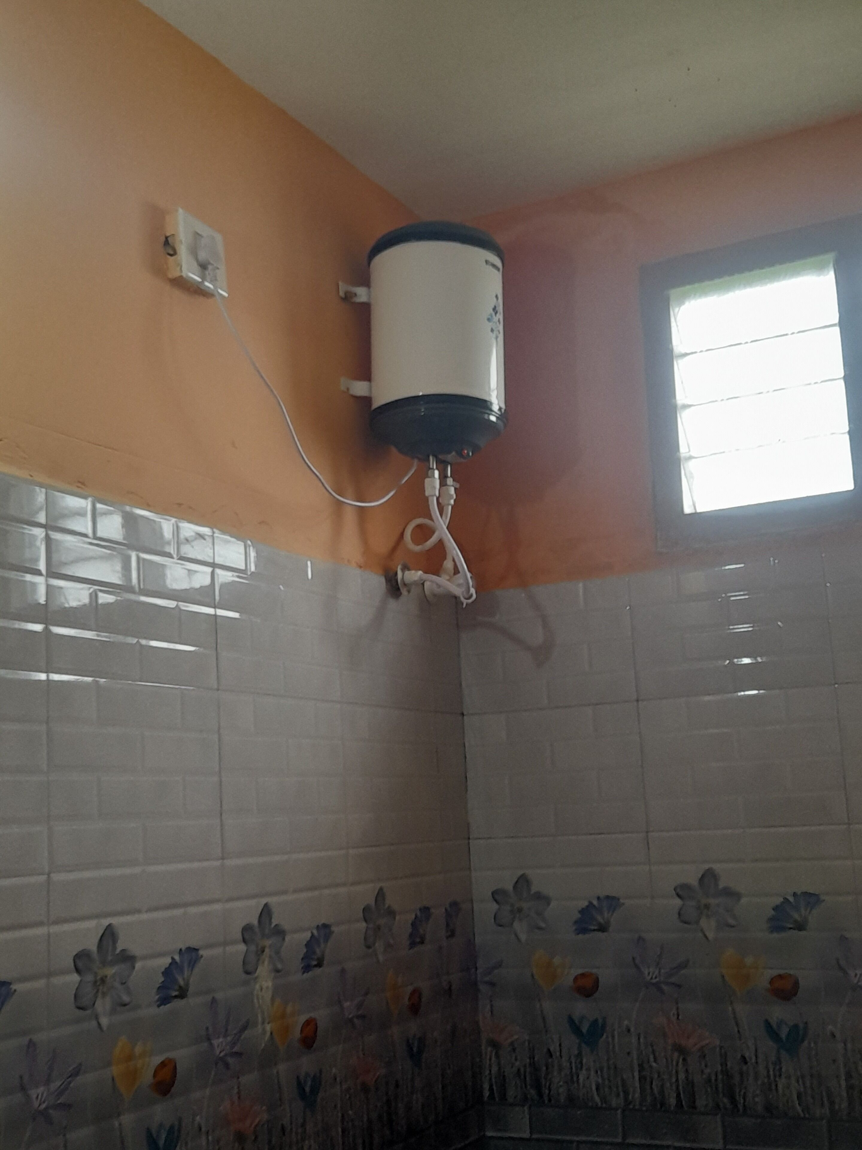 Ein Badezimmer mit Toilette, Durchlauferhitzer an der Wand und einem Fenster.