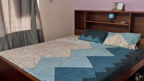 Un letto con copriletto a motivi geometrici, una testata in legno e una mensola con un mappamondo e una cornice con foto.