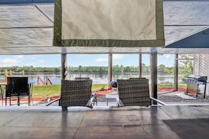 An outdoor seating area with wicker chairs, a grill, and a view of a lake.