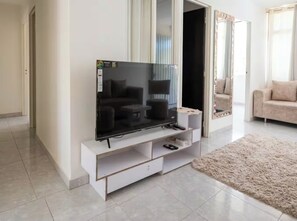 Ein modernes Wohnzimmer mit einem Flachbildfernseher auf einem weißen Standfuß, einem beigen Sofa und einem flauschigen Teppich.