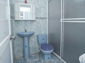 Een badkamer met een wastafel op een voetstuk, toilet en douchecabine.